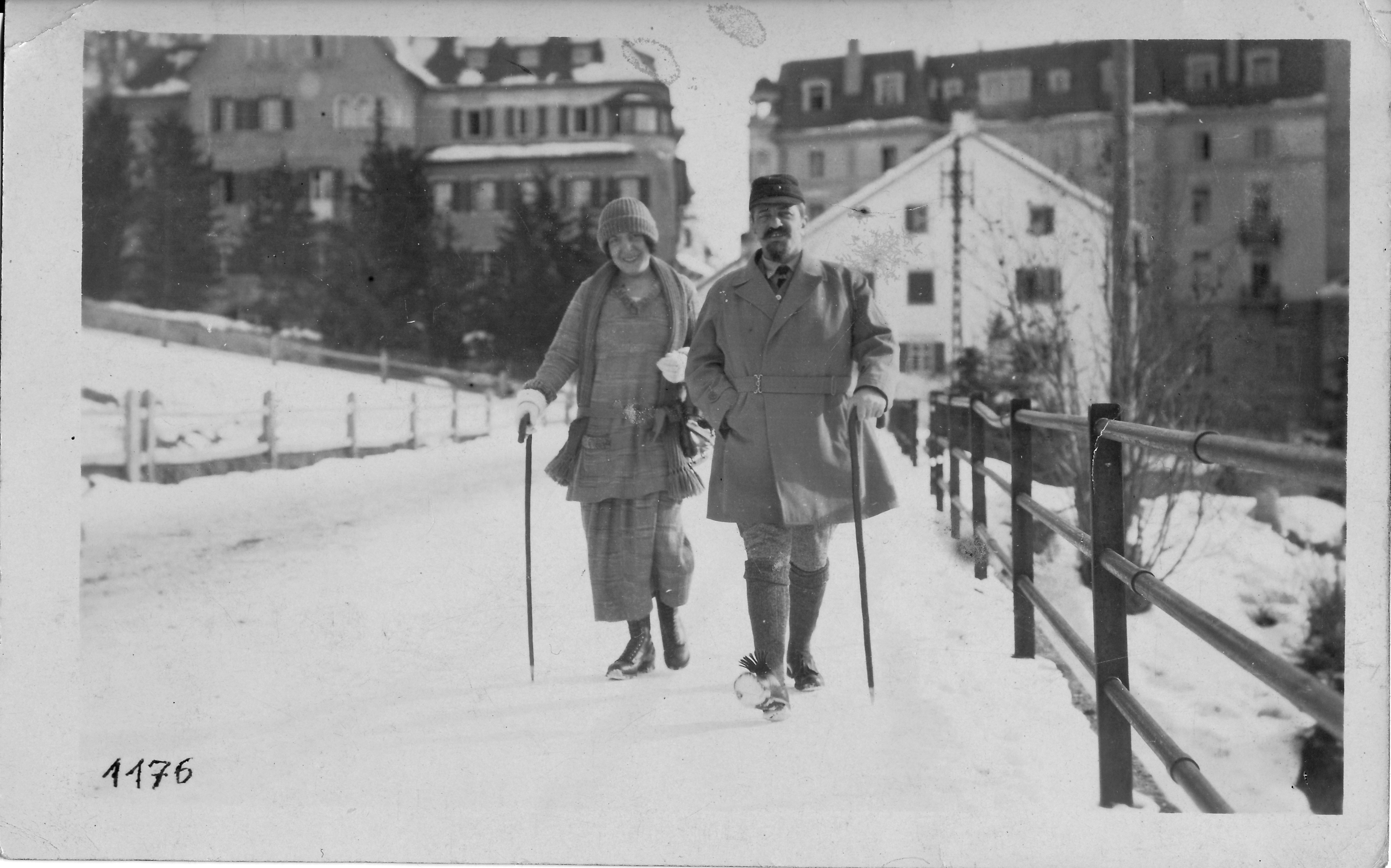 Hugo und Gertrud Simon spatzieren im Winnter mit Stöcken, im Hintergrund stehen stattliche Häuser.